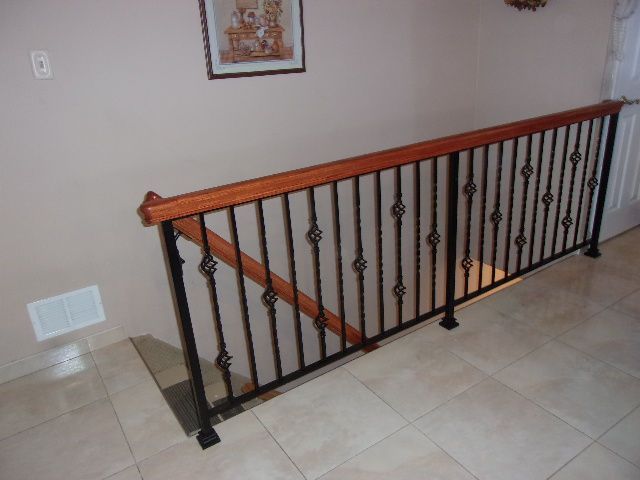 Indoor stairwell with black iron railing, wood handrail, and tiled floor.