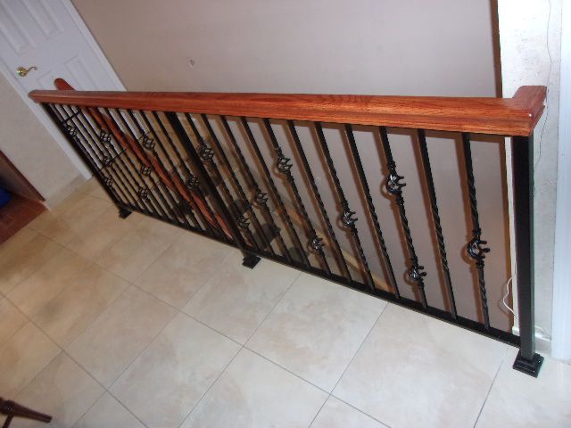 Wooden stair railing with black iron balusters along a tiled landing