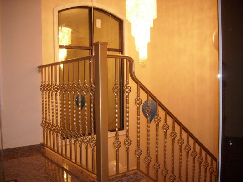 Staircase with ornate gold railings and a dark arched doorway in a warmly lit hallway