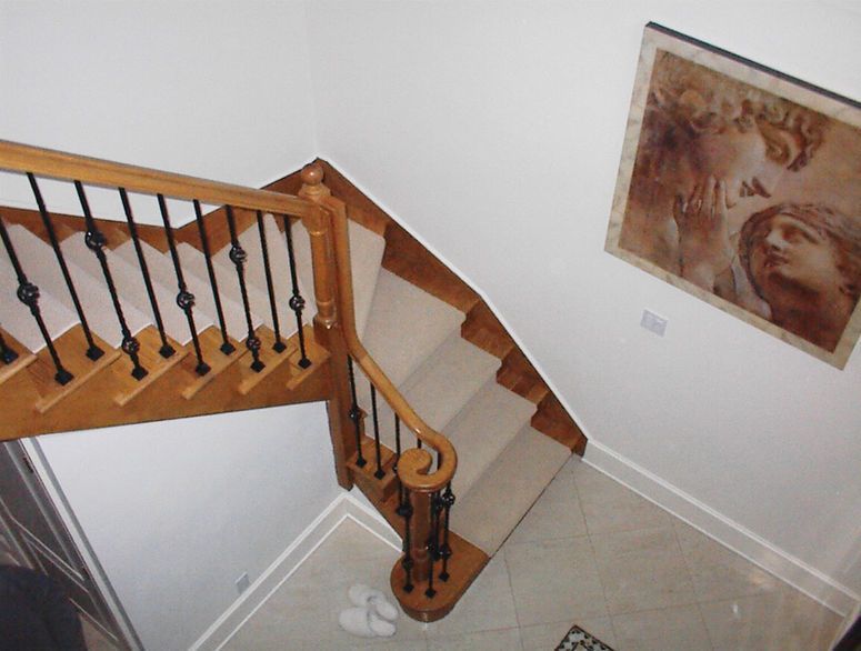 Staircase with wooden banister and black balusters in a beige-tiled foyer, wall art on the right.
