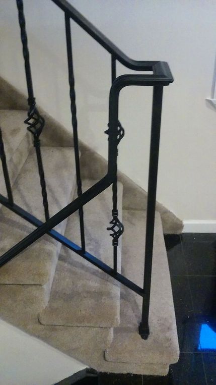Staircase with beige carpet and black metal railing beside a dark tiled floor.