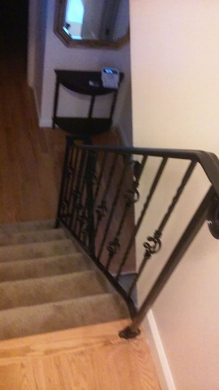 Carpeted stairway with black metal railing and wooden floor landing in a home interior.
