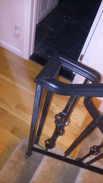 Black metal stair rail by a wood floor leading to a dark doorway