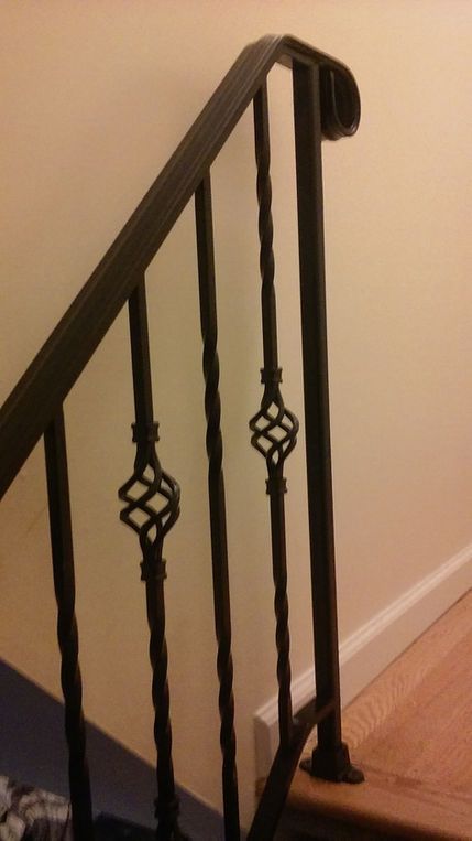 Black iron stair railing with decorative diamond details beside a wooden floor.