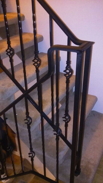 Black wrought-iron staircase railing with decorative scrolls beside beige carpeted stairs.