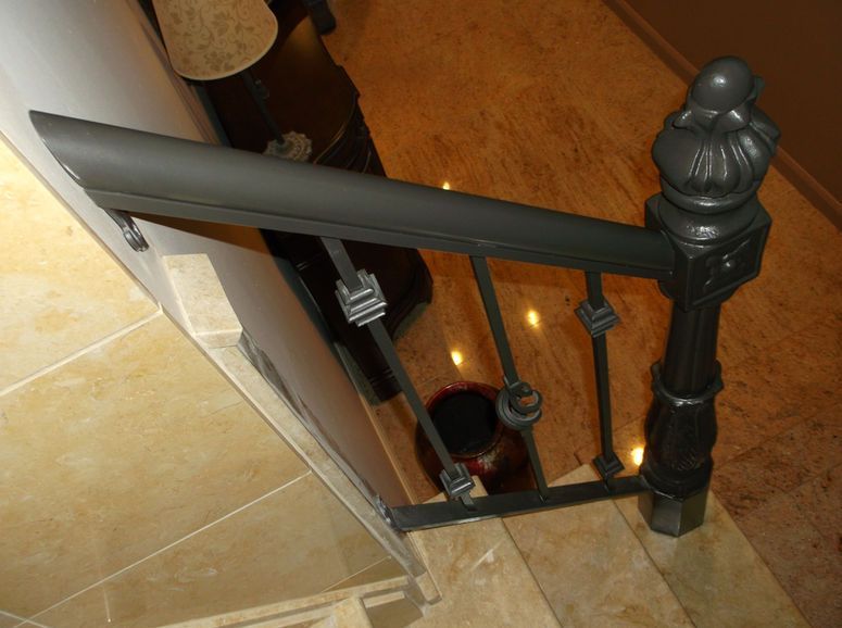 Staircase with black handrail and balusters beside tan tile and wood flooring