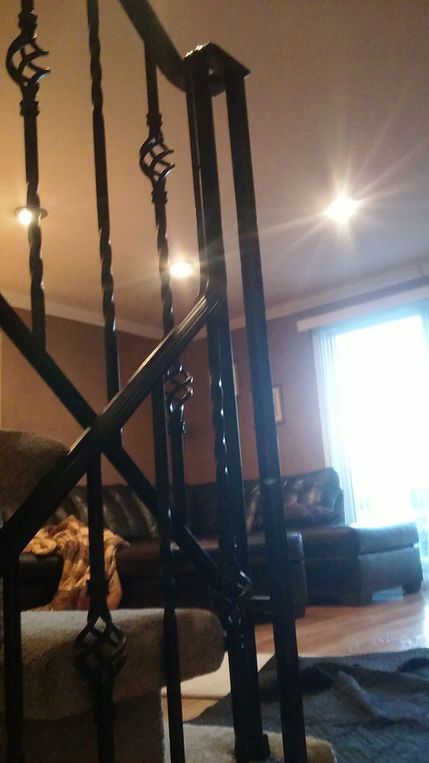 Living room with dark railing in foreground, couch, bright window, and floor lamp or ceiling light glow