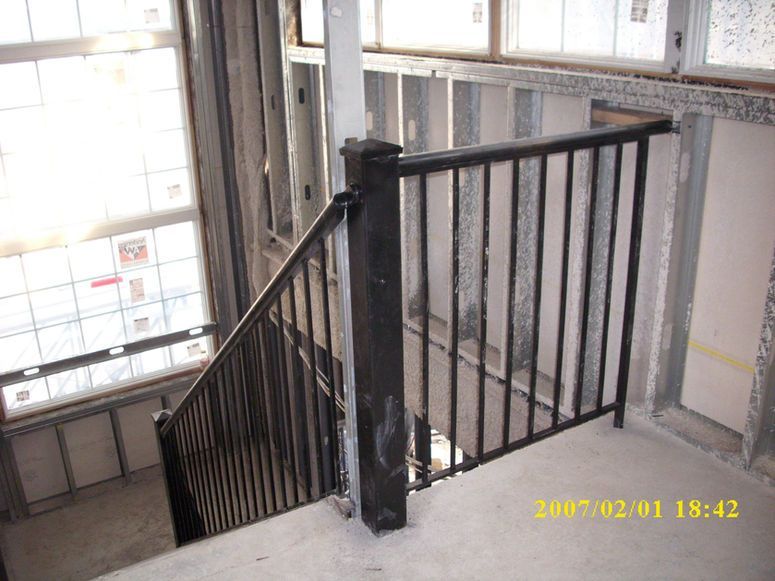 Stairwell with black metal railing beside large windows in an industrial building
