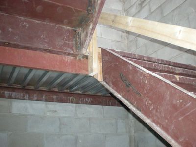 Red steel beams and corrugated metal framing against a gray cinder block wall.
