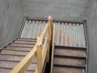 Wooden staircase inside a concrete shaft, viewed from the top looking down.