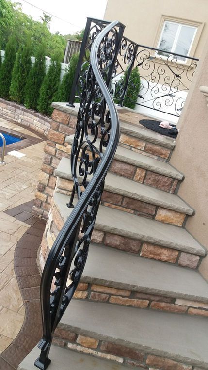 Stone outdoor staircase with decorative black wrought-iron railing beside a beige house