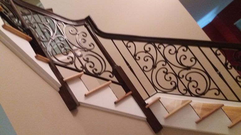 Curved staircase with ornate black wrought-iron railing and beige walls