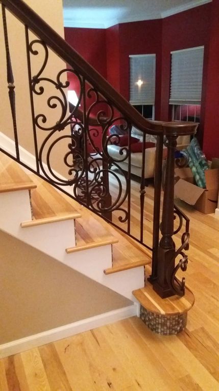 Staircase with ornate black wrought-iron railing and wood steps in a red-walled home interior