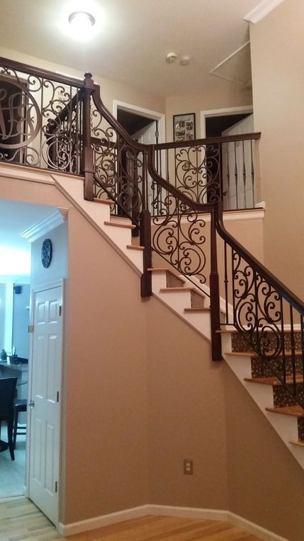Staircase with dark ornate wrought-iron railing in a beige home interior, lit by ceiling lights