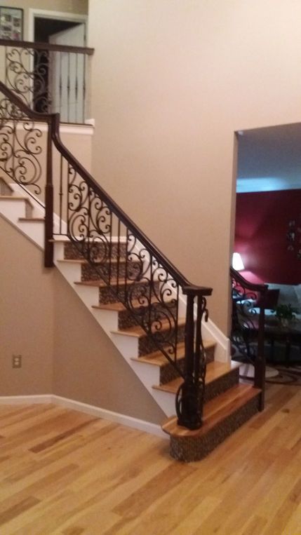 Interior staircase with ornate black iron railing and wood steps in a home foyer