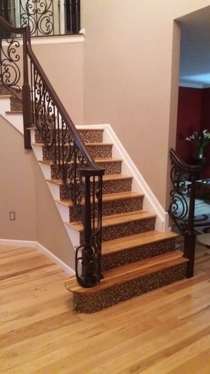 Indoor staircase with patterned carpet runner, dark wrought-iron railing, and hardwood floor.