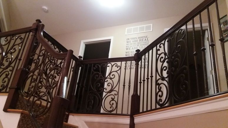 Ornate wrought-iron staircase and railing in a warmly lit interior foyer