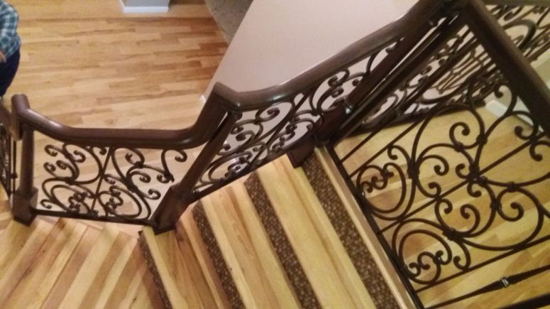 Ornate black metal stair railing beside a striped runner carpet on wooden stairs.