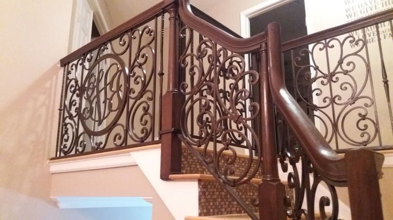 Ornate wrought-iron staircase railing with dark wood handrail in a cream-colored interior