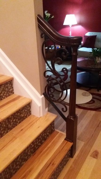 Indoor staircase with ornate black iron railing, hardwood floor, and a lit table lamp in a cozy room.