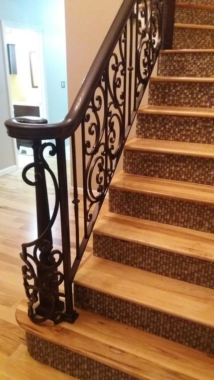 Ornate wrought-iron stair railing beside carpeted wooden stairs in a hallway