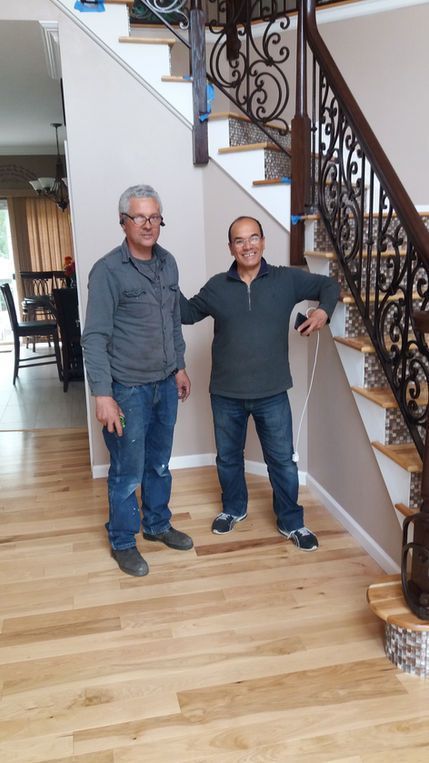 Two men standing on a wooden staircase with ornate iron railings in a home hallway
