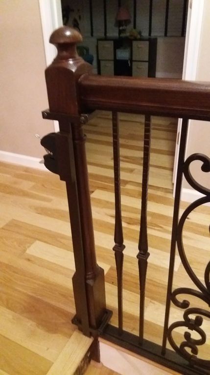 Wooden stair railing with black iron balusters beside a hardwood floor hallway