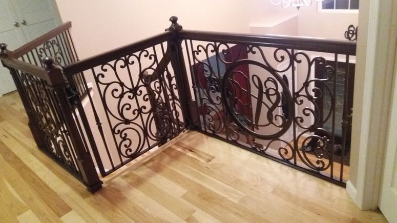 Ornate black metal stair railing around a landing with light wood flooring