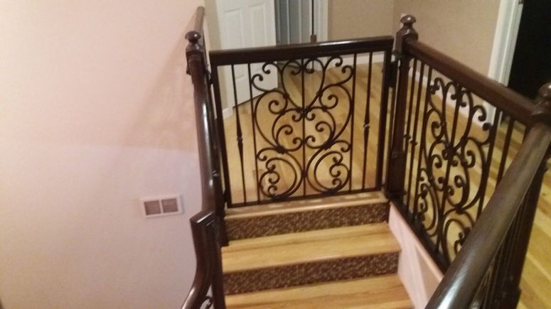 Indoor staircase with ornate black wrought-iron railing and light wood steps landing at a hallway.