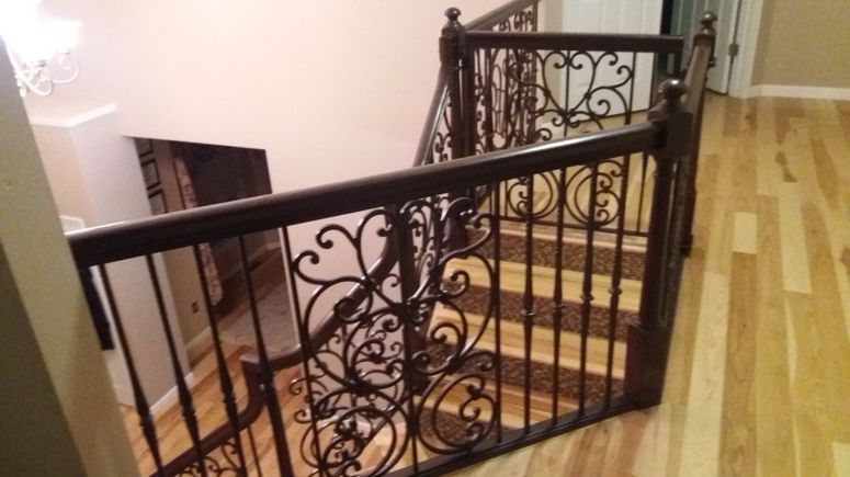 Interior stair landing with ornate black iron railing and wood flooring, viewed from above