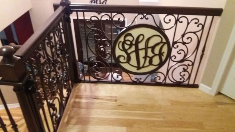Wooden staircase landing with ornate black railing and circular monogram plaque