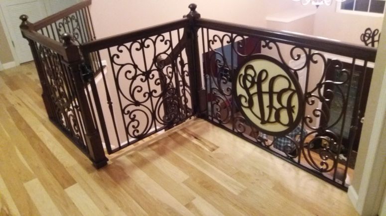 Ornate black metal stair railing on a hardwood landing with a monogrammed circular medallion