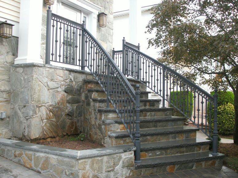 Stone exterior staircase with black iron railings leading to a house entrance