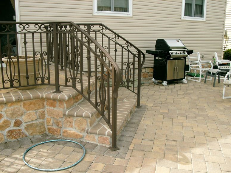 Back patio with stone steps, wrought-iron railing, brick pavers, and a grill beside outdoor chairs