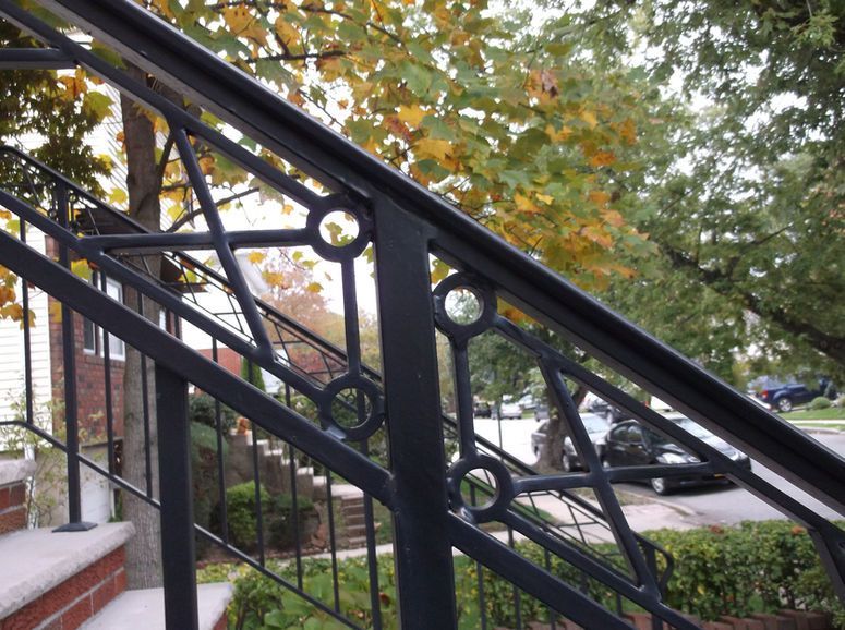 Black wrought-iron stair railing beside outdoor steps and a brick wall under leafy trees