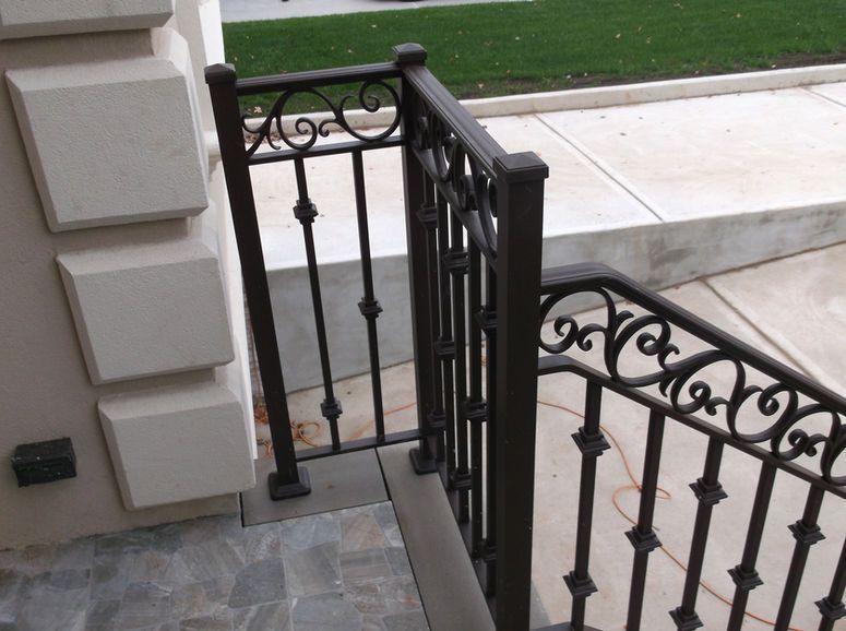 Black wrought-iron stair railing beside a stone porch and concrete walkway