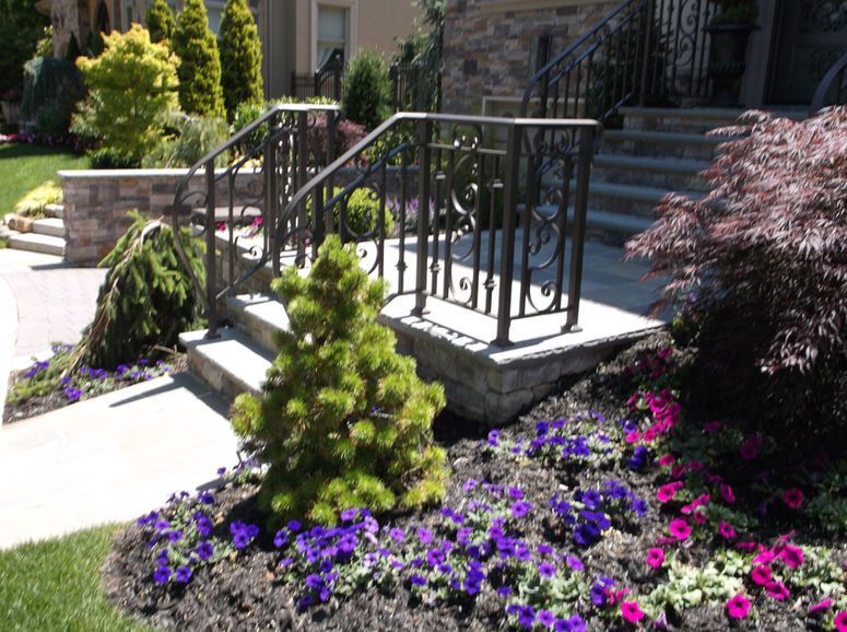 Front steps with black railing, stone landscaping, and bright purple and pink flowers in a garden.