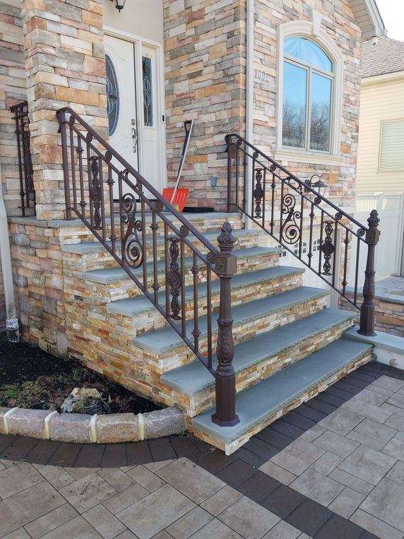 Stone front steps with black iron railings leading to a white door on a brick house.