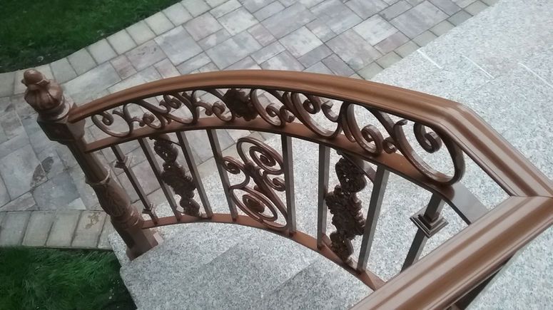 Decorative brown metal stair railing beside light gray stone steps and paved walkway