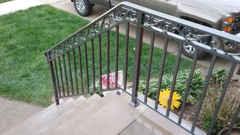 Stairway with black metal railing beside a front yard and parked truck, with flowers near the steps