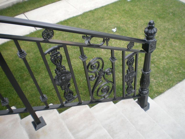 Ornate black metal stair railing beside stone steps and a green lawn