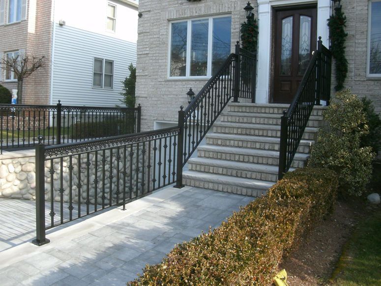 Front steps with black railings and a brick walkway leading to a house entrance