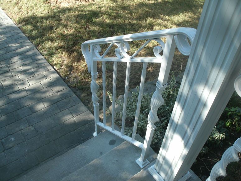 White metal porch gate beside a concrete walkway and grassy yard in sunlight