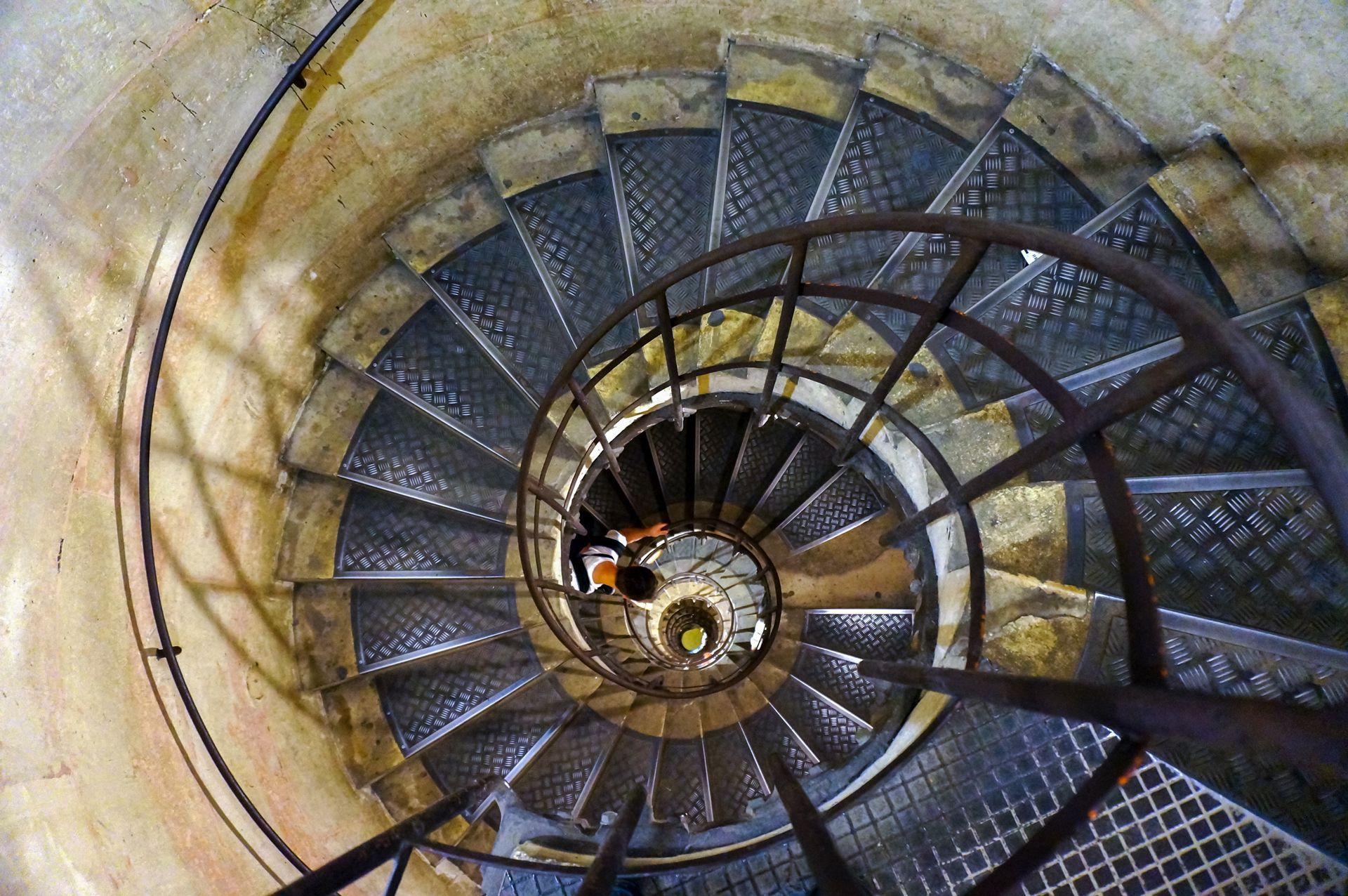 Top-down view of a spiral staircase with metal railings and worn stone steps