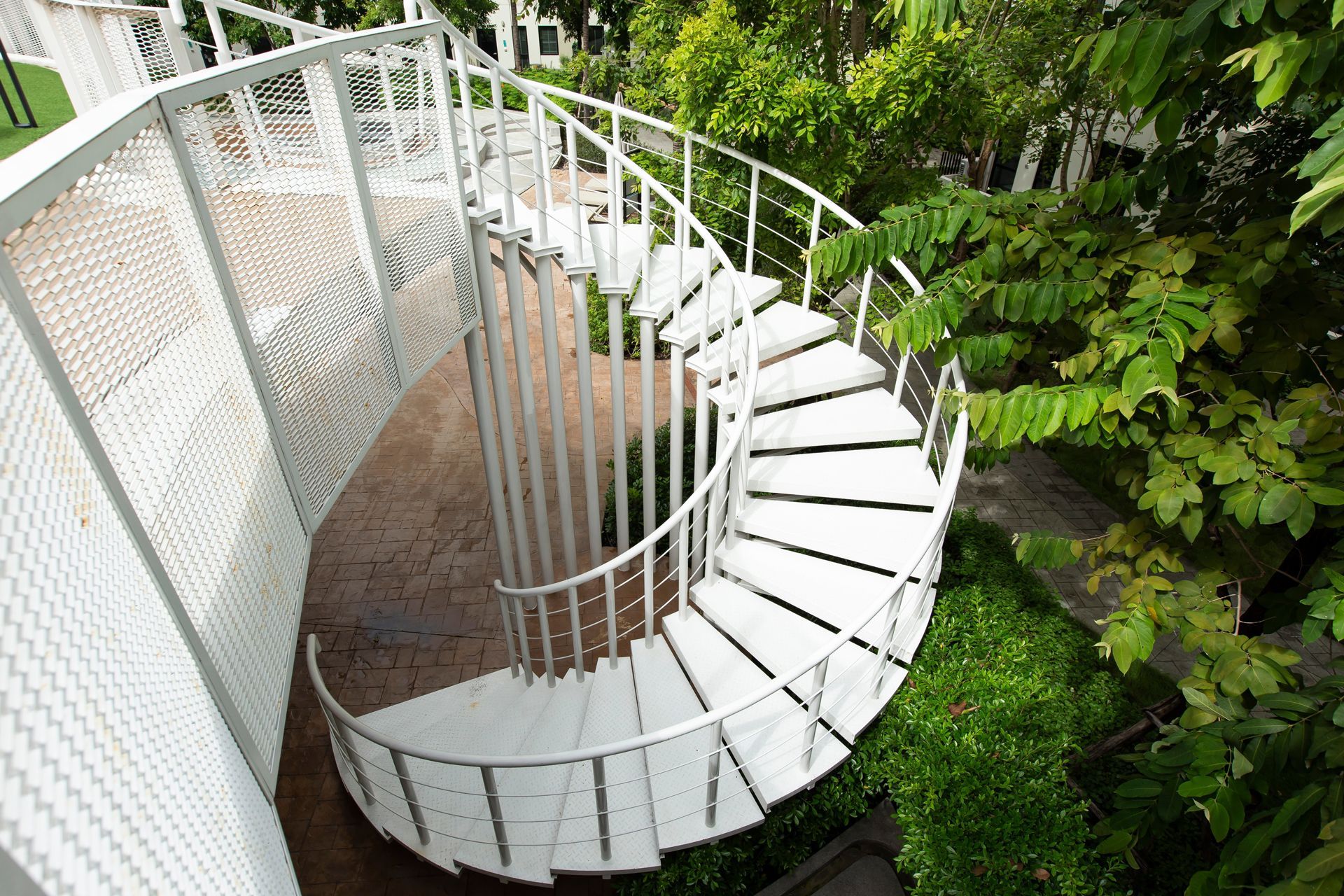 Curved white spiral staircase beside a metal fence and green foliage