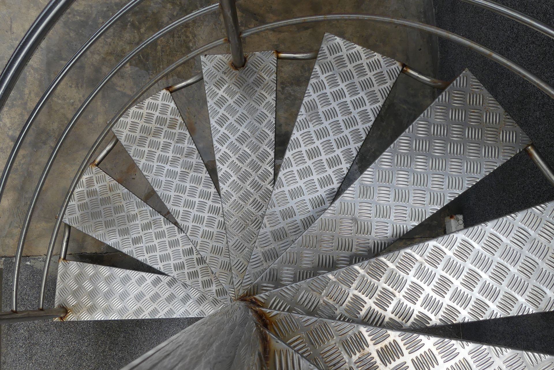Metal spiral staircase with diamond-plate steps and a curved railing, viewed from above