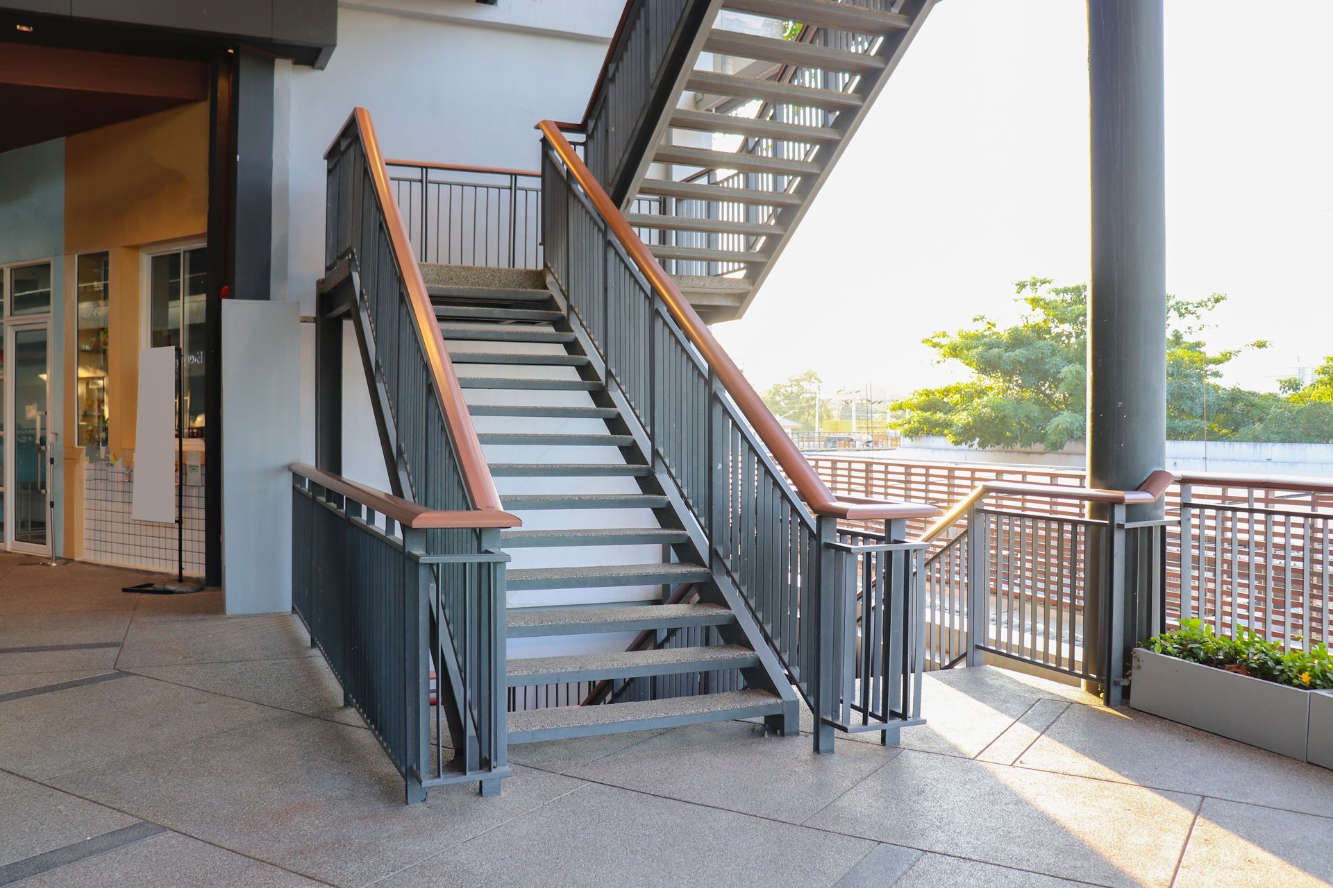 Outdoor stairway beside a building, with metal railings and a shaded walkway.