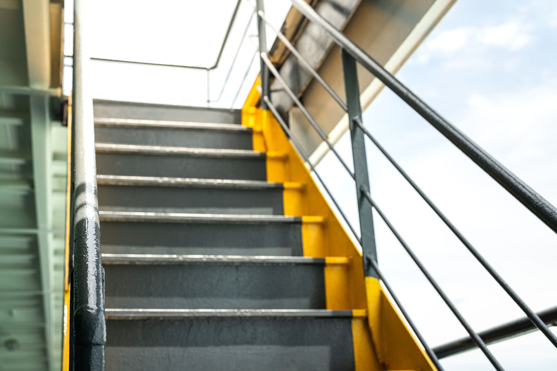 Staircase with gray steps, yellow side panels, and metal railings beside large windows