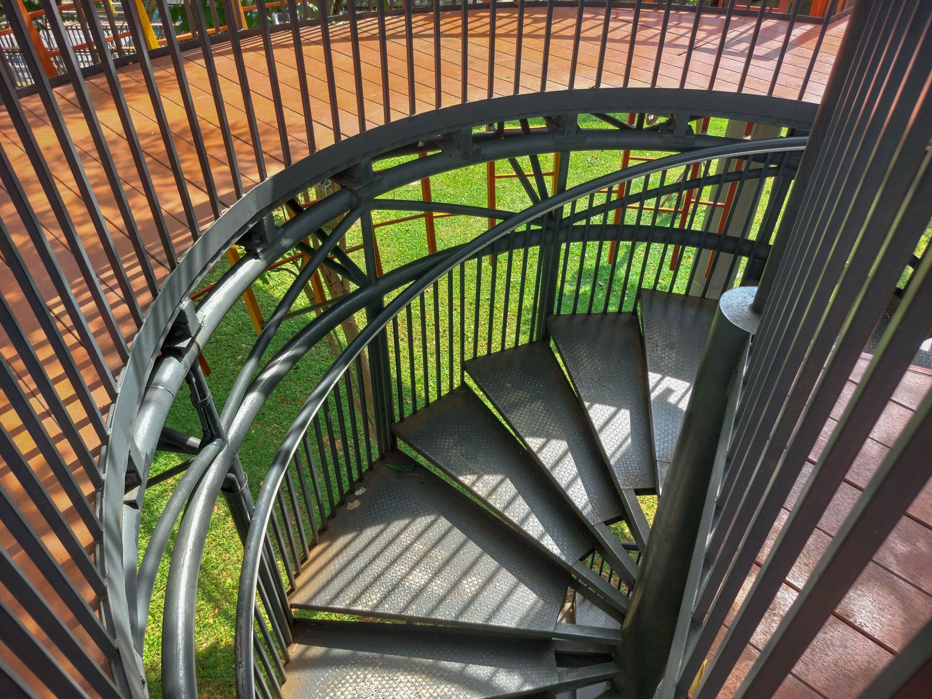 Spiral outdoor staircase with black railings and green support structure, viewed from above.