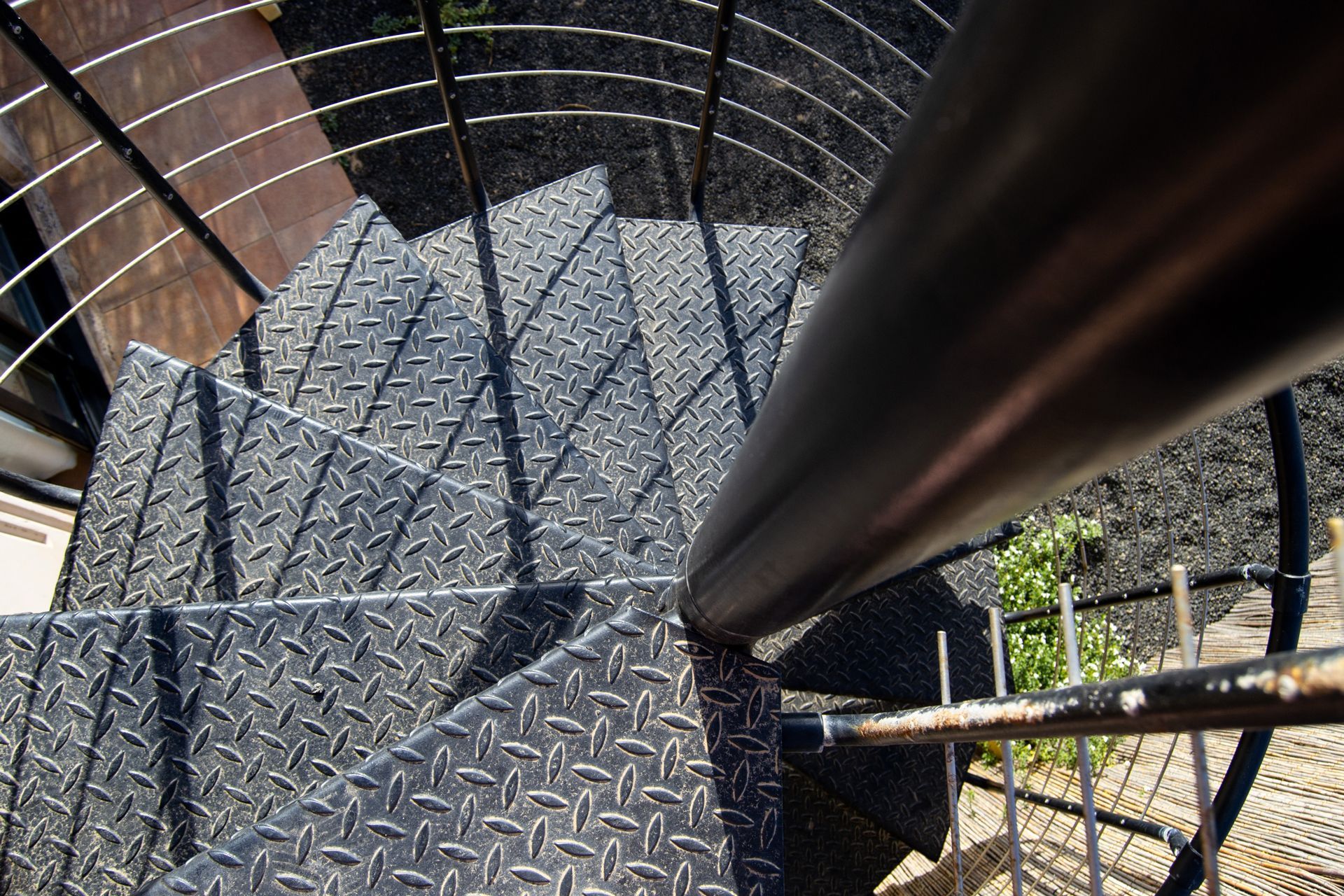 Top-down view of a spiral metal staircase with black railings and diamond-plate steps